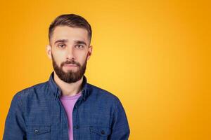 Portrait of charismatic bearded young man in casual clothes looking at camera over orange studio background. Serious millennial guy with attractive face posing, feeling calm and peaceful photo