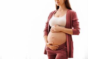 Maternity Concept. Portrait Of Young Beautiful Pregnant Lady Standing Near Window At Home, Dreamy Expectant Woman Tenderly Embracing Her Naked Belly And Smiling, Enjoying Prenatal Time, Copy Space photo