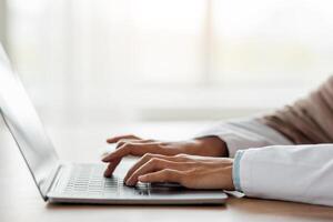 Cropped of woman doctor having online training, sitting in her cabinet, using laptop, typing on keyboard, side view, copy space. Unrecognizable lady physician working with computer, clinic interior photo