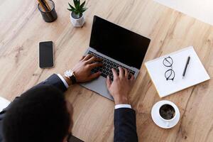 Top view of african american businessman typing on modern laptop with empty screen, black manager working online in his office, having online conference or call with business partners, mockup photo