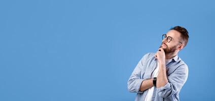 Pensive Caucasian guy thinking over decision or problem, looking at empty space over blue studio background. Thoughtful bearded man hoping, imagining,making choice photo