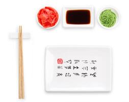 Set of sushi tablewear. Top view on empty rectangular sushi plate with hieroglyphs, saucer, ginger, wasabi and chopsticks at white background. Flat lay, copy space photo
