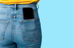 Cropped view of female having cellphone with blank screen in jeans pocket on blue studio background, mockup for mobile app or website. Free space for your advertisement template photo
