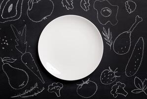 Hand drawn food on chalkboard and empty white plate, top view. Mockup for restaurant menu with copy space on platter photo