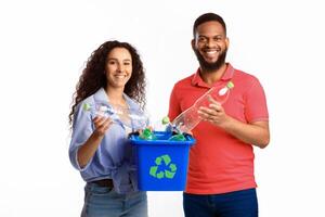 Recycling And Waste Sorting. Diverse Couple Holding Box With Recycle Symbol And Used Plastic Bottles Standing Over White Studio Background. Junk Disposal Concept photo