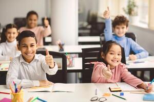 Education Is Fun Concept. Diverse group of happy smiling international classmates sitting at desks in classroom and showing thumbs up sign gesture, children enjoying studying at junior school photo