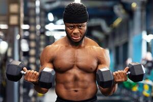 Muscular black guy doing workout with dumbbells at gym, lifting weight with both hands, copy space. Motivated african american man bodybuilder working on biceps, weight exercises concept photo