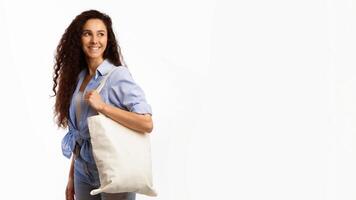 No Plastic. Happy Woman Carrying Flax Eco Bag Posing Looking Aside On White Studio Background. Eco-Friendly Shopping, No Plastic Life, Ecology Concept. Panorama With Copy Space photo