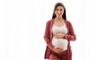 Expectation Concept. Portrait Of Happy Young Woman Embracing Her Pregnant Belly While Standing Near Window At Home, Beautiful Expectant Lady Touching Tummy And Smiling At Camera, Copy Space photo