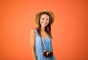Going vacation. Happy woman tourist with camera and summer hat posing over yellow studio background, copy space. Young excited lady photographer getting ready before travelling, smiling at camera photo
