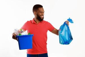 African American Millennial Man Holding Garbage Bag And Box With Recycle Symbol And Wasted Plastic Standing In Studio Over White Background. Sort Your Waste Concept photo