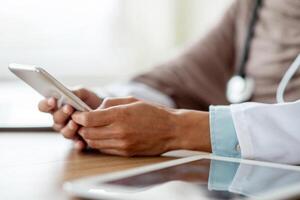 Cropped of female doctor using gadgets at workplace, holding smartphone and digital tablet. Unrecognizable therapist having online conversation with her patients, using mobile phone, closeup photo