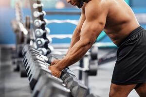 Shirtless african american muscular bodybuilder grabbing dumbbell at modern gym, copy space. Handsome black athletic man working out with dumbbells, making work out with weights photo