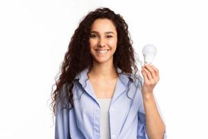 Happy Woman Showing Energy-Saving Light Bulb Posing Standing In Studio On White Background, Smiling To Camera. Lightbulbs Disposal, Energy-Saving Lightbulb Concept photo