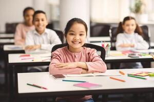 Elementary Education. Portrait of happy small asian girl sitting at table in classroom at primary school with group of classmates and posing, looking at camera and smiling. Studying And Learning photo