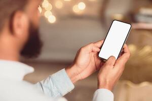 People And Technology Concept. Over The Shoulder View Of Unrecognizable African American Man Using Smart Phone With White Empty Screen For Mockup, Sitting At Home, Making Call Or Chatting photo