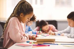 Portrait of small black girl with afro braids sitting at table in classroom at primary school or kindergarten, writing or drawing in notebook. Reopening and return back to school after lockdown photo