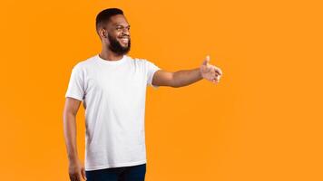 Side View Of Black Man Stretching Hand For Handshake Greeting Aside Standing Posing Over Yellow Studio Background. Nice To Meet You, Shaking Hands Greeting Gesture Concept. Panorama, Free Space photo