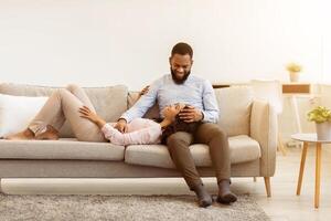 Free Time Together. Happy beautiful african american couple spending weekend on the couch indoors at home in living room, relaxing and enjoying the company of each other, woman lying on man's lap photo