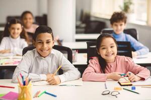 Education And Children Concept. Portrait of happy smiling diligent boy and girl sitting at table in classroom at elementary school with group of classmates in background and posing, looking at camera photo