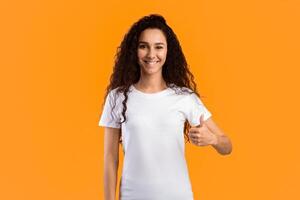 I Like It. Smiling Lady Gesturing Thumbs Up Smiling To Camera Posing Standing On Yellow Background, Studio Shot. Woman In White T-Shirt Showing Thumbs-Up Gesture Approving Something photo