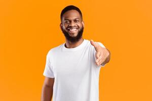Hello. Happy African American Man Offering Hand For Handshake To Camera Standing Over Yellow Background. Deal, Nice To Meet You Concept. Shaking Hands Greeting Gesture Concept. Studio Shot photo