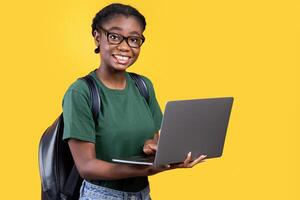 Happy Black Student Girl Using Laptop Computer Posing Smiling To Camera Standing Over Yellow Background. Studio Shot. E-Learning And Online Education. Educational Gadgets Concept photo