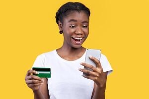 Shopping. Joyful African American Lady Using Phone Holding Credit Card, Shops Online Via Mobile App Standing On Yellow Background. Studio Shot. Shopping Application Concept photo