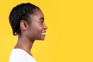 Profile Portrait Of African American Young Woman Smiling Looking Aside At Copy Space Posing Over Yellow Studio Background. Side View, Advertisement With Happy Black Female And Blank Space For Text photo