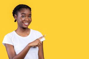 Look There. Smiling African Woman Pointing Finger Aside At Free Space Advertising Your Text Standing On Yellow Studio Background. Check This Out Concept. Advertisement Banner. Panorama photo