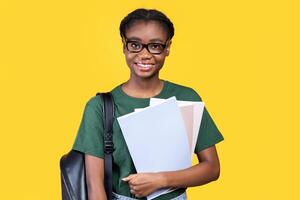 Happy Black Female Student Posing With Books And Notebooks Standing On Yellow Studio Background, Smiling To Camera. College And University Education, Students Lifestyle Concept photo