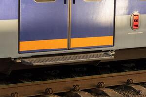 Metallic train doors stand ready for travelers, bathed in soft, golden light as dusk approaches. Trackside greenery adds a touch of tranquility to the calming atmosphere of the station photo