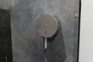A modern restroom features a round silver paper dispenser affixed to a blue textured wall. This practical fixture is designed for easy access and convenience for users photo