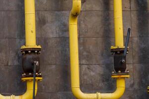 Yellow gas pipelines run along a weathered gray wall, unveiling a blend of modern engineering and industrial aesthetics. Valves create connections, reflecting the energy system's intricate design photo