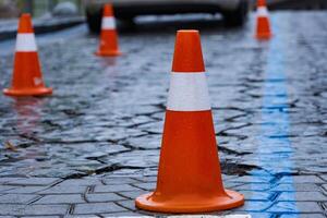 Glimmering rain-soaked cobblestones are lined with vibrant orange traffic cones, indicating ongoing construction while pedestrians carefully navigate through the busy city environment photo