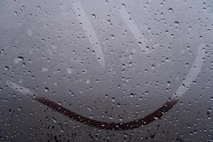 Delicate raindrops cling to a glass surface, blurring the world outside. A joyful smile traced through the mist captures the whimsy of a dreary day, enhancing the cozy atmosphere inside the vehicle photo