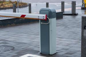 A parking barrier stands tall at an urban setting, controlling vehicle entry with its smooth, modern features. The grey pavement reflects a muted sky, highlighting the meticulous design photo