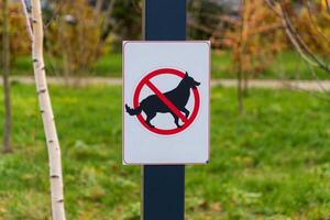 A clear warning sign stands in a lush outdoor space, featuring a graphic of a dog crossed out by a red circle photo