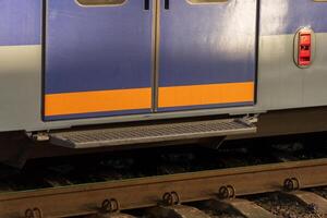 Brightly colored electric train doors stand open, ready for passengers at a bustling railway station. The morning sun casts soft shadows on the platform, inviting commuters to board photo