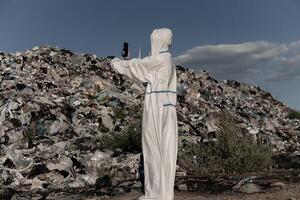 A person dressed in protective gear surveys a sprawling landfill, capturing the overwhelming sight of plastic waste and debris affecting the ecosystem under a clear sky photo