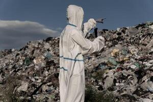 In a vast landfill, a person dressed in protective gear points towards a heap of garbage, highlighting the urgent need for effective recycling and waste management strategies photo