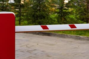 An automatic barrier gate stands closed, effectively controlling entry into a parking lot. The red and white design complements the lush greenery, ensuring safety and organization photo