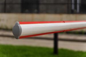 A red and white barrier gate stands firmly at the entrance of a parking lot, creating a clear boundary. The gate emphasizes security and control, enhancing safety for vehicles and pedestrians photo
