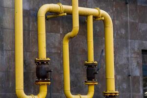 Bright yellow gas pipes wind along a concrete wall, showcasing the intricate connections of energy transportation. Industrial components hint at a complex infrastructure that powers cities photo