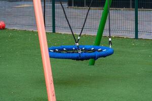 A colorful blue swing hangs in a lively public park, surrounded by soft grass, inviting children to experience joy and fun in their outdoor playtime photo
