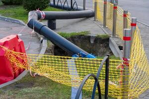 Construction workers are repairing a water pipeline at an urban site, with safety barriers and digging equipment visible surrounding the exposed section of the pipe photo