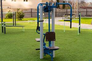A piece of fitness training equipment stands ready for use in an outdoor gym, surrounded by green grass and other exercise areas, providing a healthy lifestyle option for the community photo