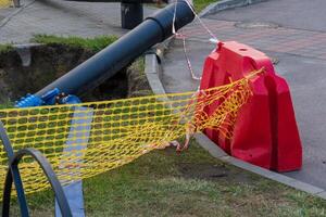 Construction crews are repairing a damaged water pipeline at a site. They are digging near a barrier, ensuring safety with warning tape and equipment at the location photo
