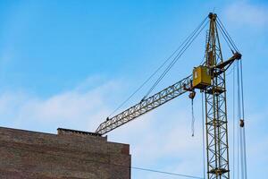 A construction crane stands tall against a blue sky, overseeing a building site. Workers are engaged in activities to complete the structure, emphasizing industrial growth in the city photo