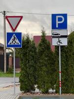 Several road signs stand at an intersection, displaying a pedestrian work zone symbol and designated parking for vehicles and handicapped access. The setting reveals nearby greenery and urban scenery photo